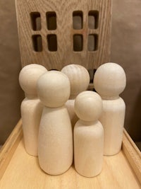 five wooden dolls on a tray in front of a wooden house